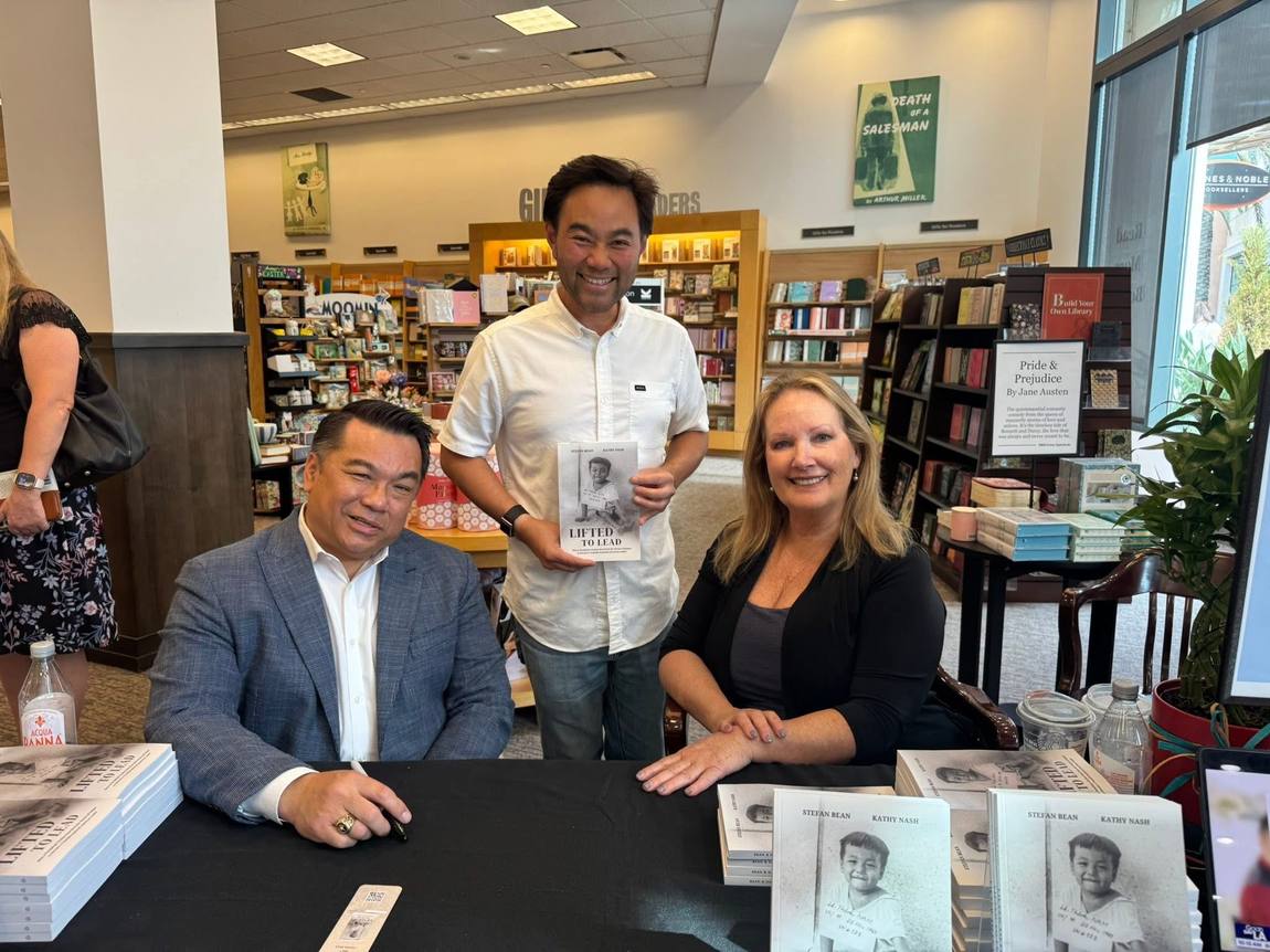 Dr. Bean at a signing table in a bookstore with two readers, stacks of the book in front of them